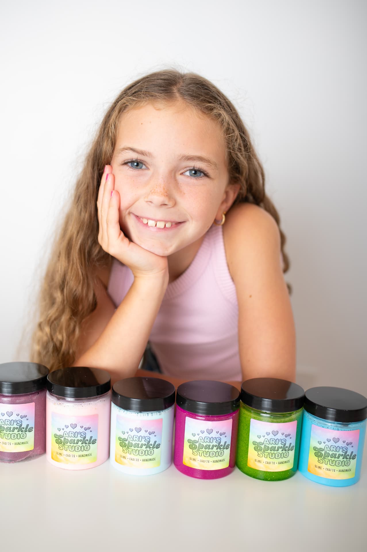 Ari with a row of colorful Ari's Sparkle Studio slime jars